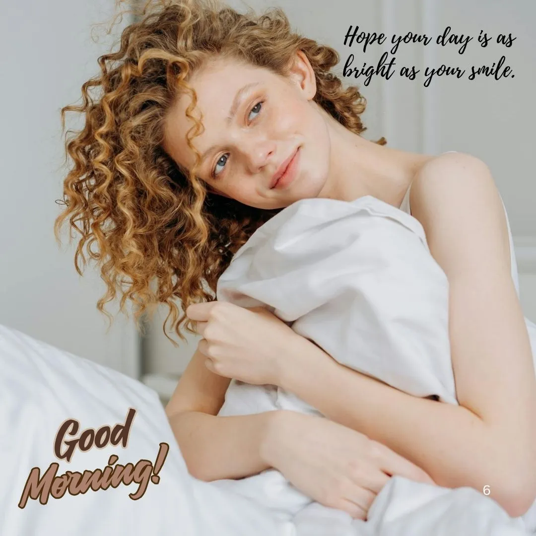 Bright Morning Smiles – Good Morning Message with Warm Wishes Smiling curly-haired woman in bed holding blanket with “Good Morning” and a positive message on image